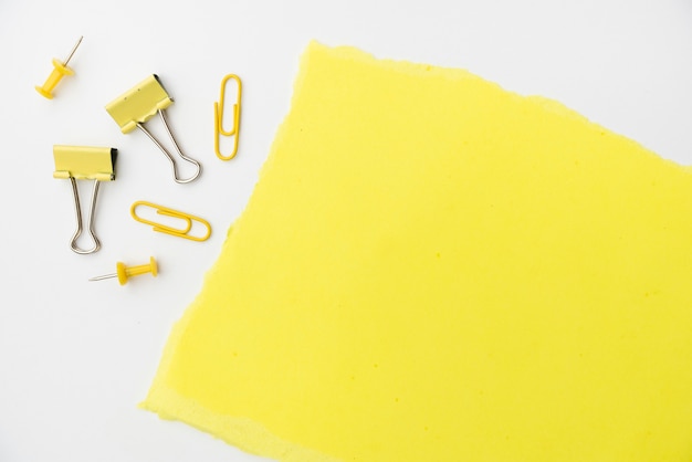 Бесплатное фото Желтая крафт-бумага с скрепкой и канцелярской кнопкой на белом фоне