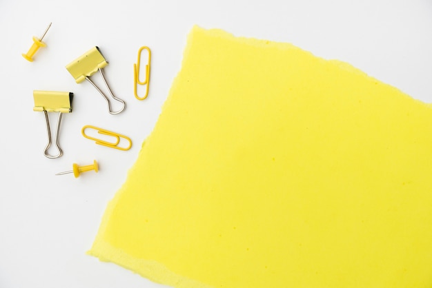 Yellow craft paper with paperclip and pushpin on white backdrop