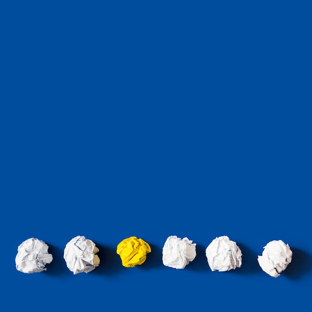 Foto gratuita palla di carta sgualcita giallo fra le palle bianche contro fondo blu