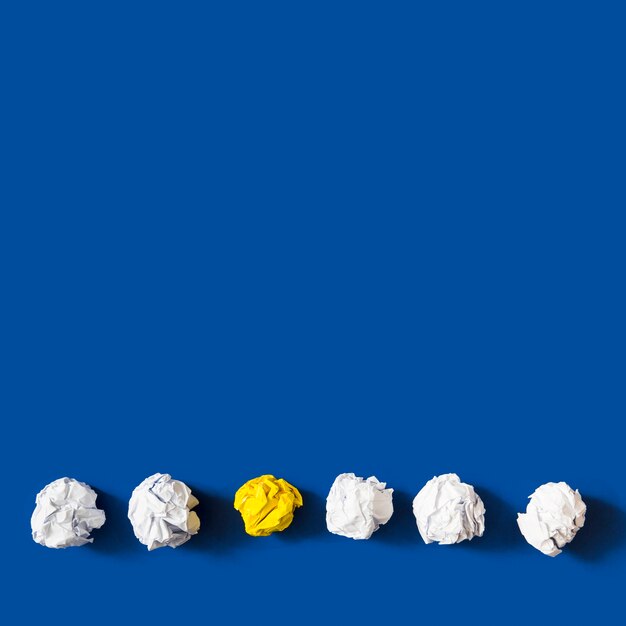 Yellow crumpled paper ball among the white balls against blue background