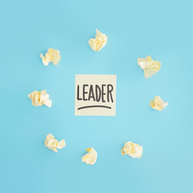 Yellow crumpled paper surrounded around leader text adhesive note on blue backdrop