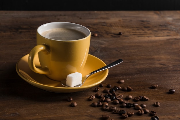 Yellow cup of coffee and plate with sugar cube