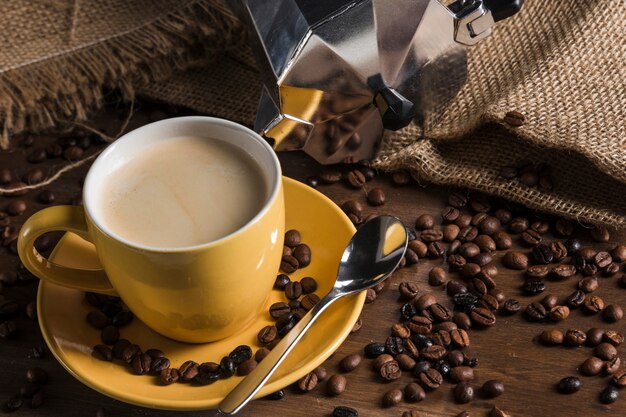 Yellow cup near scattered coffee beans and sackcloth