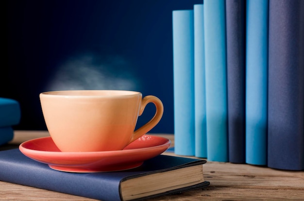 Желтая чашка кофе или чая с горячим паром на книге светло-голубые книги и синий фон