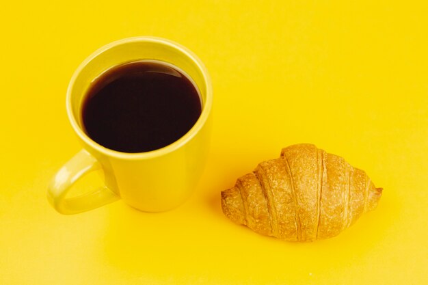Yellow cup with coffee and croissant on a yellow background