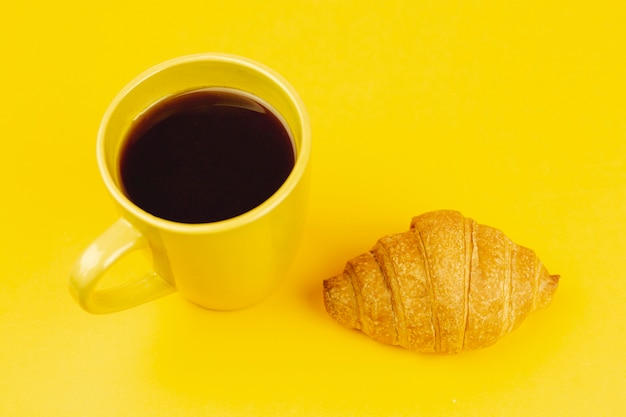 コーヒーとクロワッサンが黄色の背景に黄色のカップ