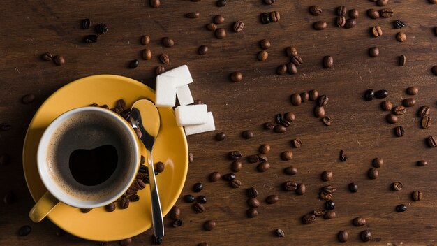 Yellow cup with plate and sugar blocks near coffee beans