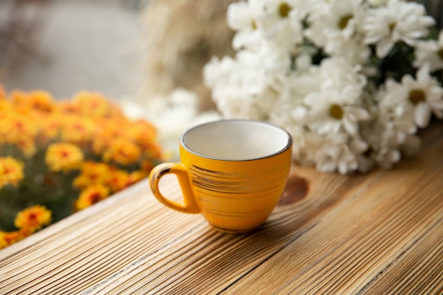 Yellow cup on a wooden surface on a blurred background with flowers