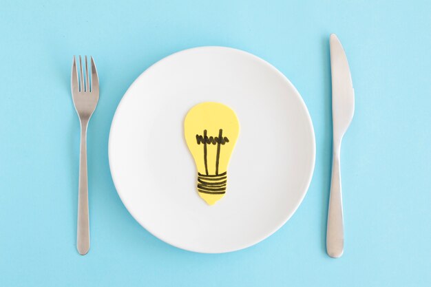 青い背景にフォークとバターナイフと白板の黄色のカットアウト電球