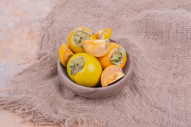 Yellow date plums in a wooden cup on burlap.