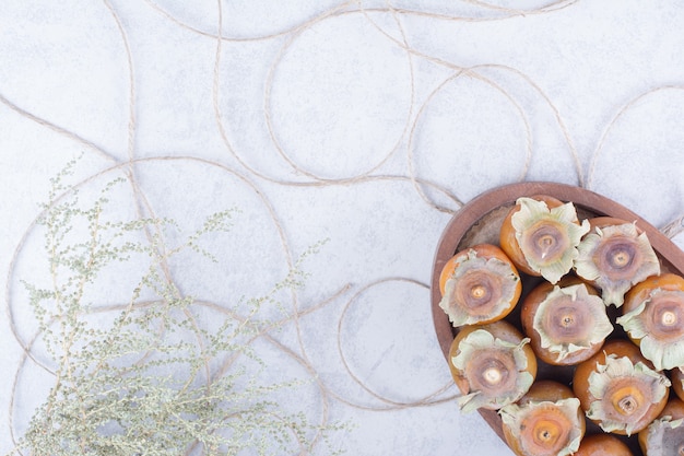 Yellow date plums in a wooden platter on grey.