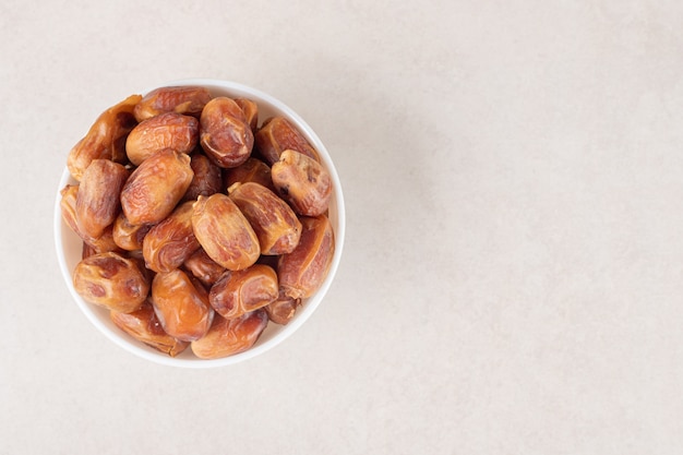 Free photo yellow dry dates in a ceramic cup on concrete.