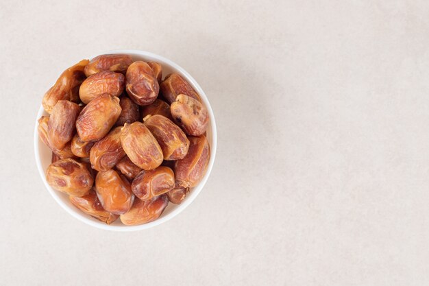 Yellow dry dates in a ceramic cup on concrete.