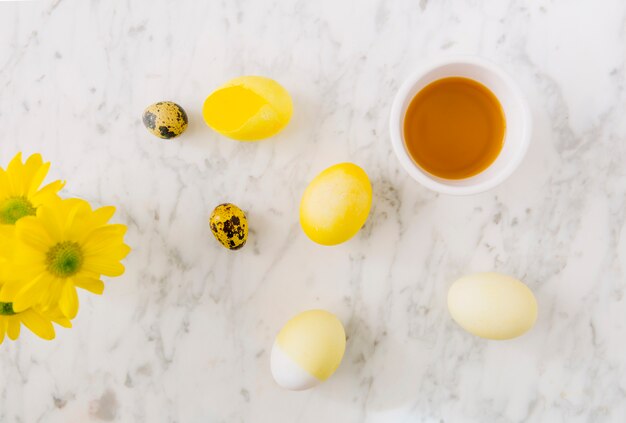 Yellow Easter eggs near fresh flowers and dye liquid