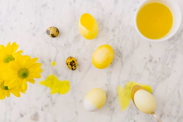 Yellow Easter eggs near fresh flowers, spoon and dye liquid