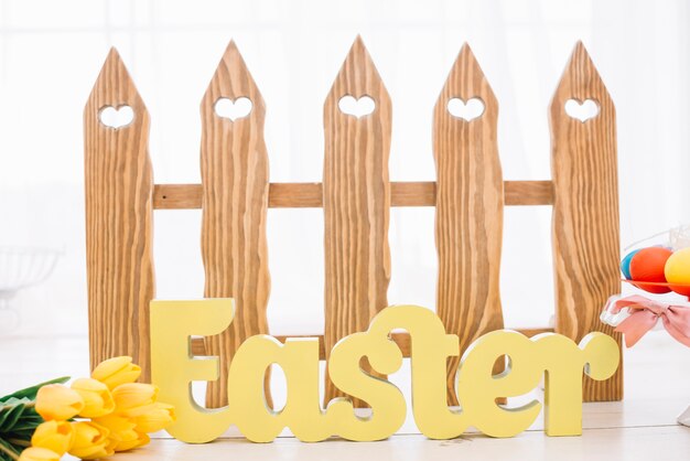 Yellow easter word in front of wooden heart shape fence with tulip flowers