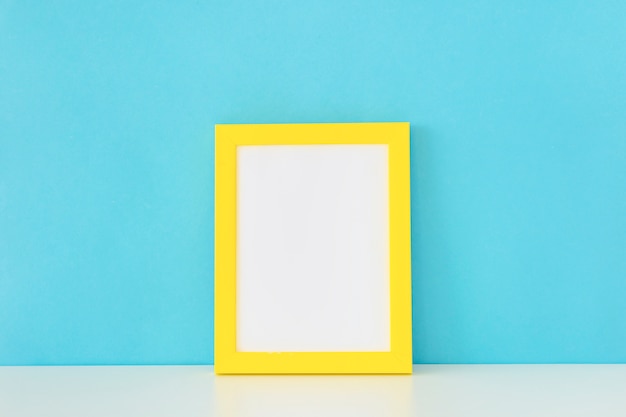 Yellow empty photo frame in front of blue wall