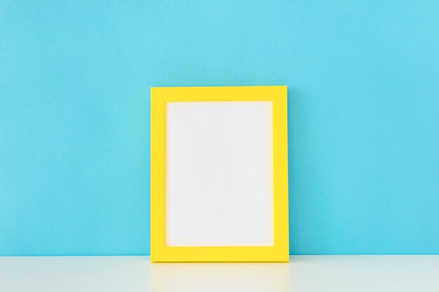 Yellow empty photo frame in front of blue wall