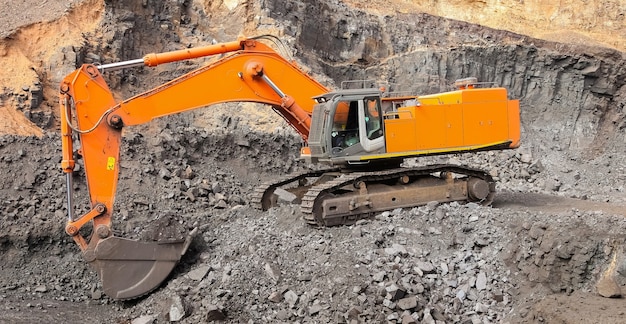 Yellow excavator digging for ore rich rock in an open pit mine