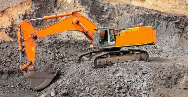 Yellow excavator digging for ore rich rock in an open pit mine