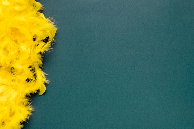 Yellow feather boa on blue background with copy space