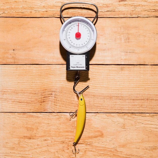 Yellow fishing bait hanging on measuring scale over the wooden desk