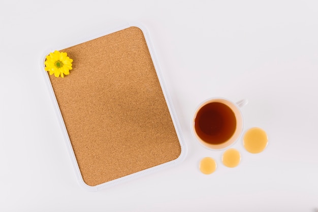 Yellow flower on cork frame near tea and honey drops over white surface