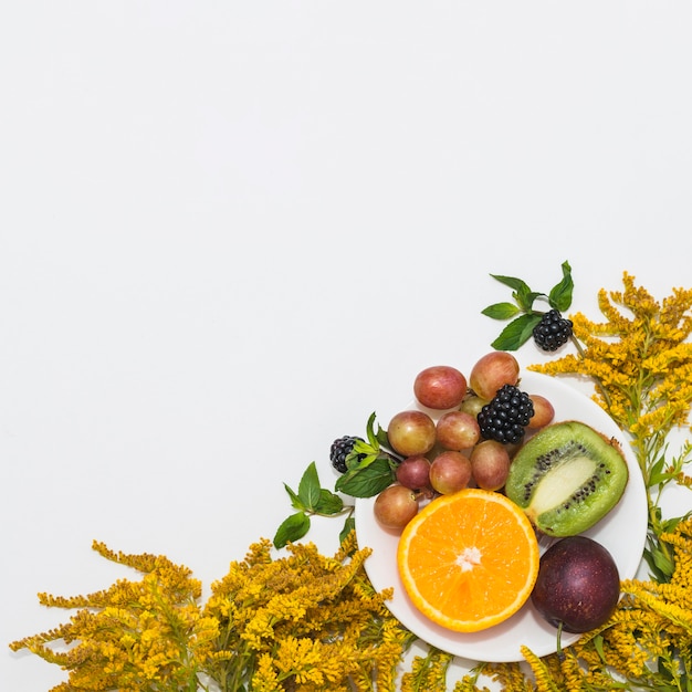 Free photo yellow flowers with fruits on plate against white background