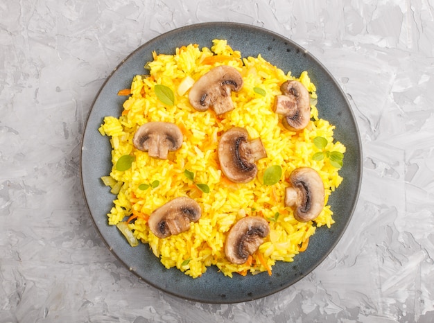 샴 피 뇽 버섯, 심 황 및 오 레가 노 회색 콘크리트 표면에 블루 세라믹 접시에 노란색 볶음밥. 평면도.