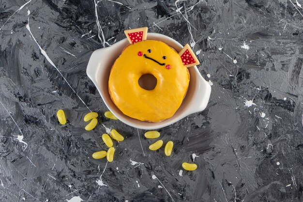 Yellow glazed doughnut with beans candies placed on a marble table.