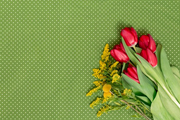 Yellow goldenrod and red tulip flowers on corner of green polka dot background