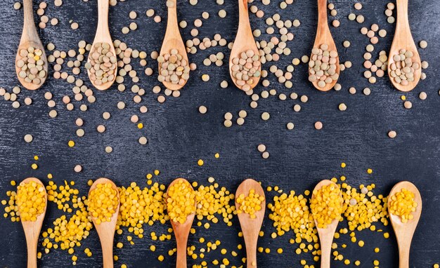 Yellow and green lentils in a wooden spoons on a black stone table. top view.