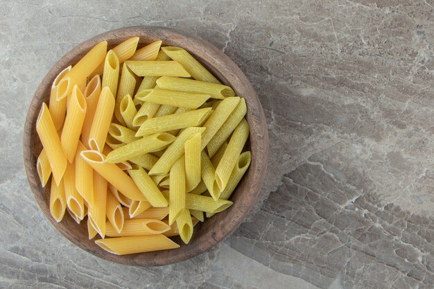 Yellow and green penne pasta in wooden bowl