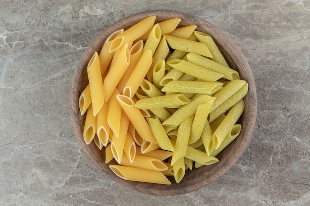 Yellow and green penne pasta in wooden bowl