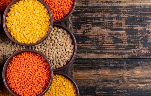 Yellow, green and red lentils in a brown bowls close-up on a dark wooden table