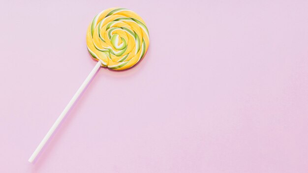 Yellow and green striped lollipop against pink background