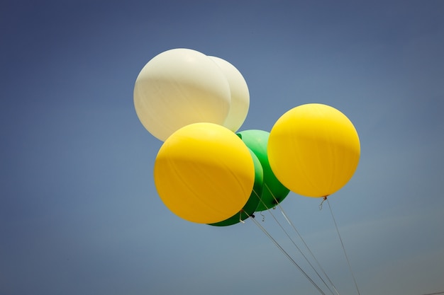 黄色、緑色、白い風船が空を飛ぶ