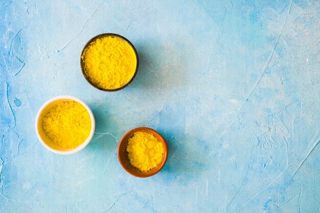 Yellow holi color powder in the different type of bowls on blue painted backdrop