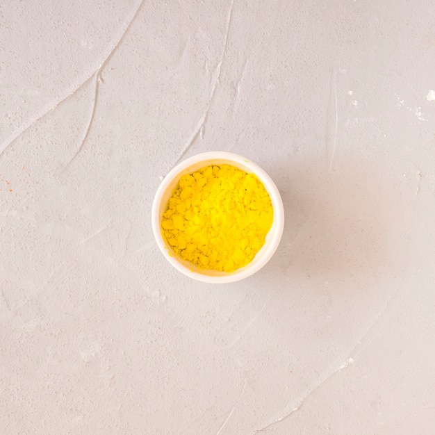 Желтый Холи цветной порошок в белой миске на бетонном фоне