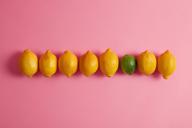 부드러운 풍미와 분홍색 배경에 대해 행에 하나의 녹색 라임 노란색 육즙 레몬. 소화기 건강을 개선하고 체중 감량을 돕는 섬유질이 풍부합니다. 건강한 과일 개념