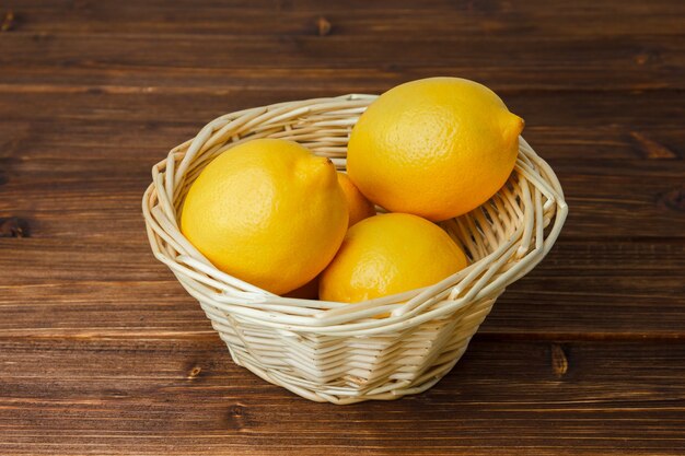 Yellow lemons in a basket on a wooden surface. high angle view.