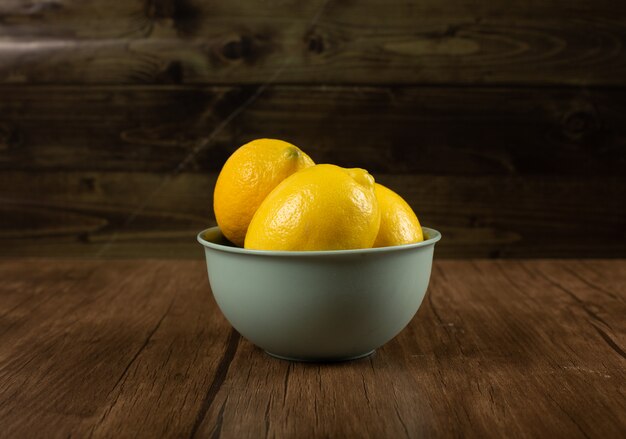 Yellow lemons in a bowl on wooden table