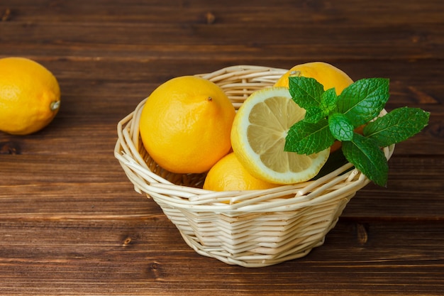 Yellow lemons and green leaves in a basket with sliced lemon high angle view on a wooden surface