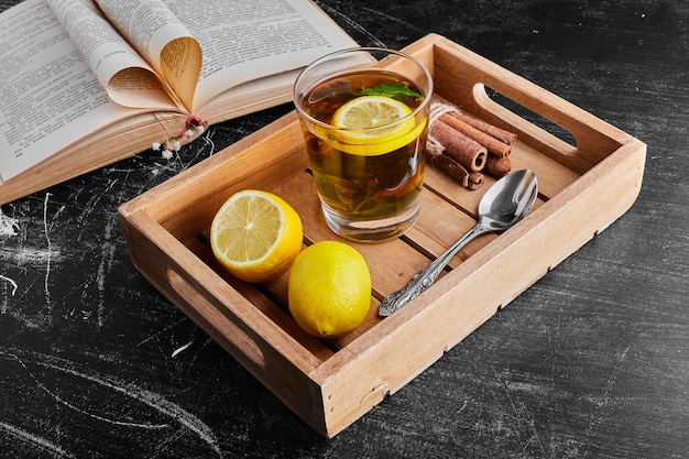 Yellow lemons isolated on black surface with a glass of drink in a wooden tray. 