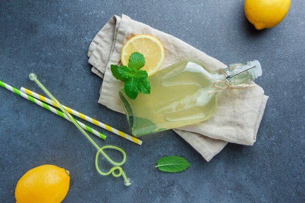 Yellow lemons with lemon juice on white fabric cloth and straws flat lay on a white surface