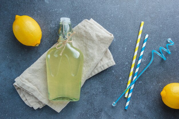 Yellow lemons with lemon juice on white fabric cloth and straws flat lay on a white surface