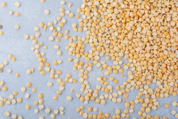 Yellow lentil messily scattered over marble background.