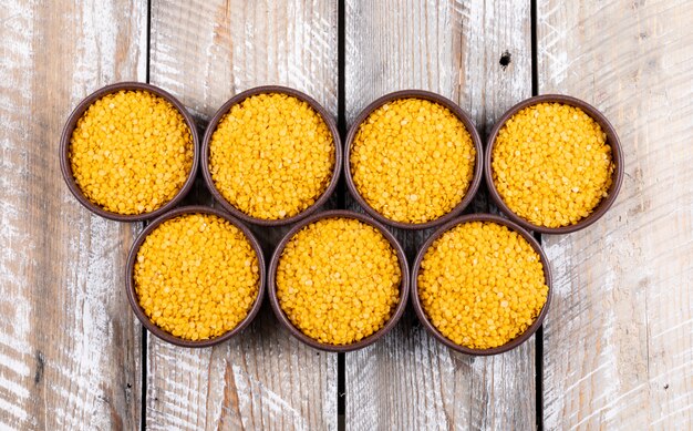 Yellow lentils in a brown bowls on a beige wooden table. top view.