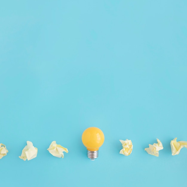 Yellow light bulb with crumpled papers on blue background