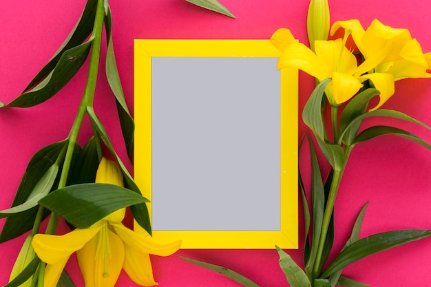 Free photo yellow lily flowers and blank picture frame over the pink; background